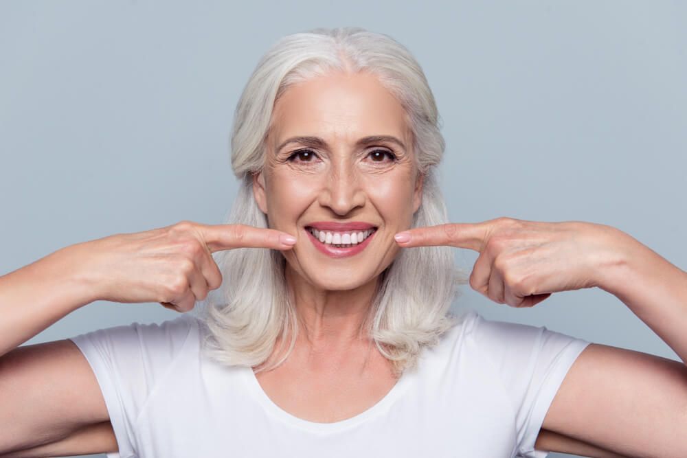 Senior woman in white shirt pointing to her teeth