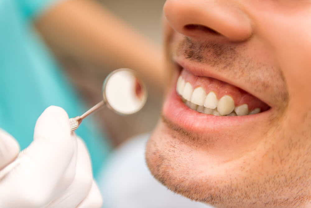 Holding a dental mirror near a male patient's mouth