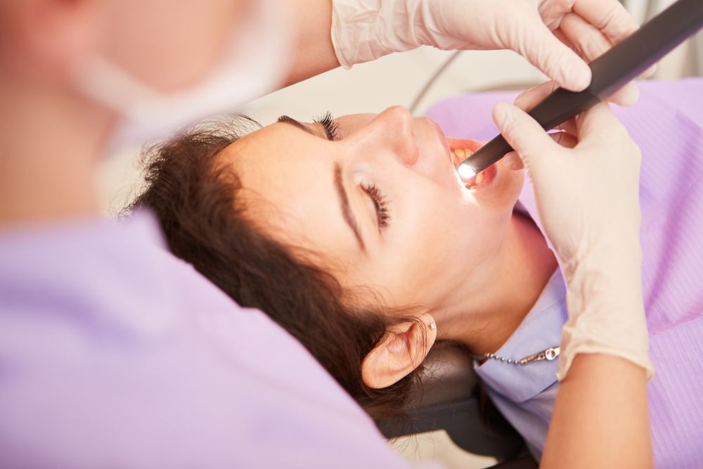 Cosmetic dentist looking at woman´s teeth with a light