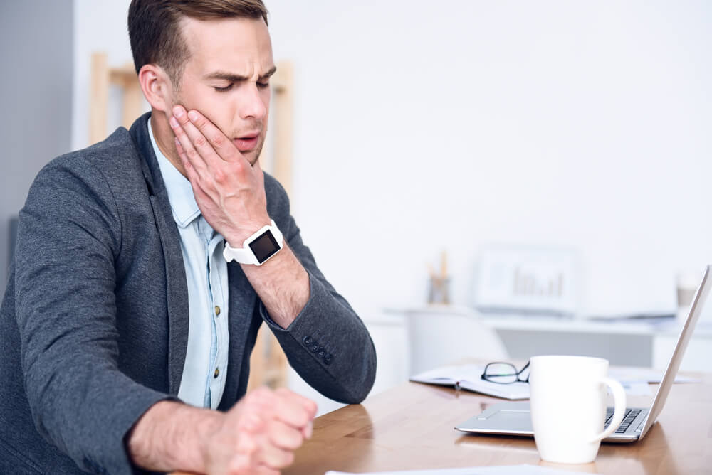 Man at his office holding his jaw in pain from trismus