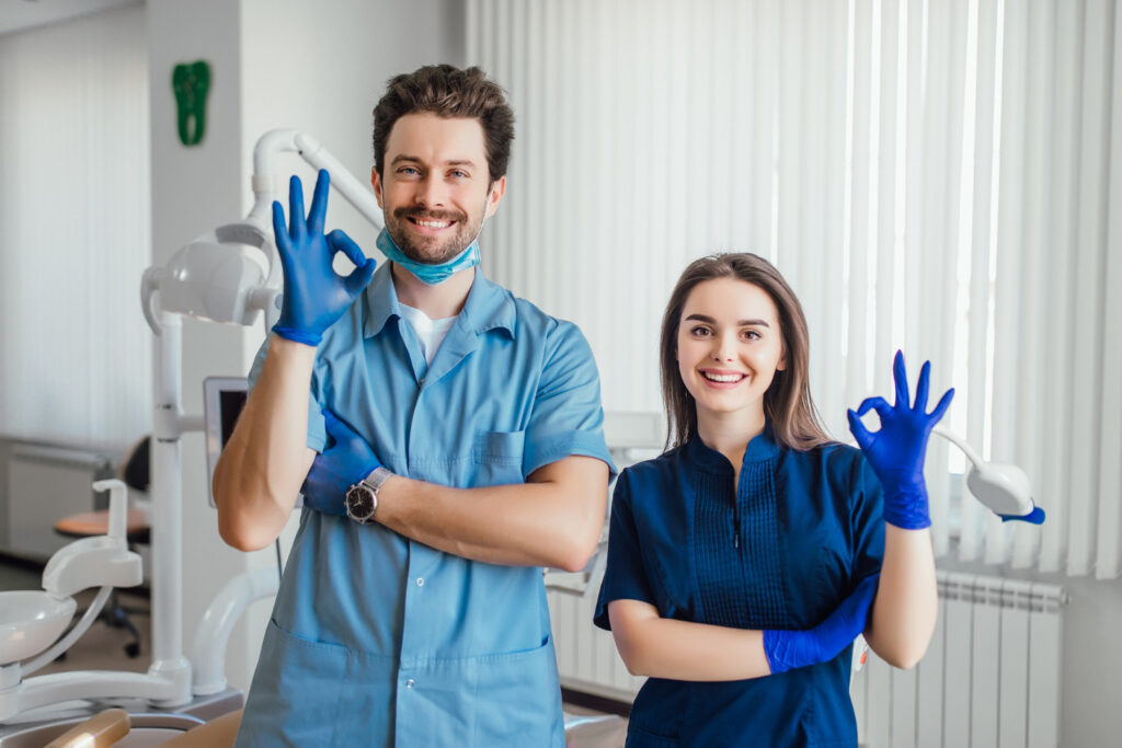 Two dental technicians at Toothbar smiling and giving the A-OK sign, symbolizing excellent patient care and service quality.