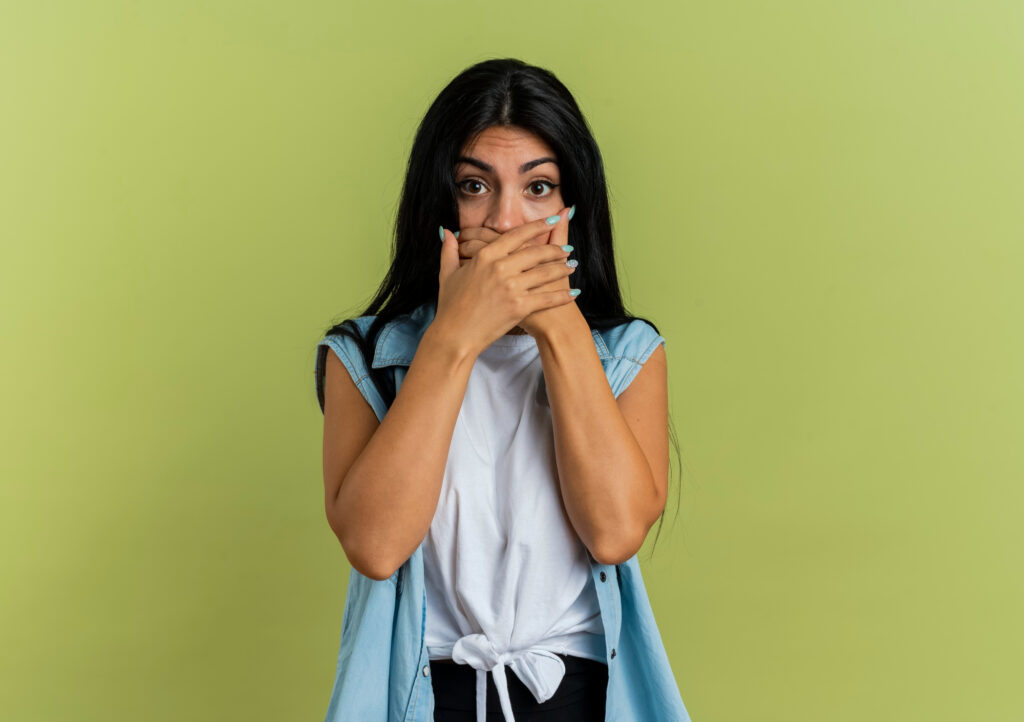 Woman covering her mouth with her hand against a green background, depicting anxiety or discomfort related to dental issues