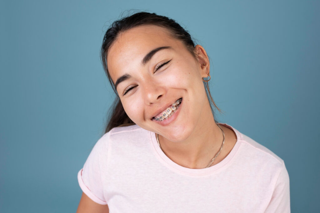 Young woman smiling broadly, showcasing traditional braces, against a vibrant blue background, highlighting her orthodontic treatment