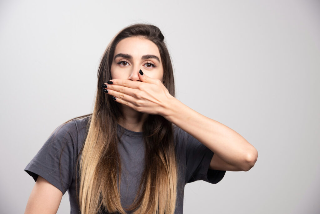 Woman covering her mouth with her hand, feeling embarrassed about her smile, depicting dental self-consciousness.