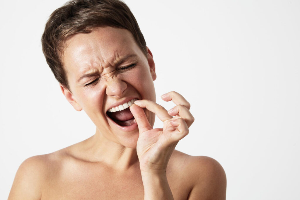 Woman examining a chipped tooth in her mouth, showing concern for her dental health