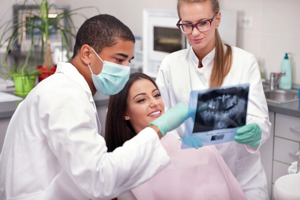 Patient looking at X-ray flanked on both sides by dental staff.