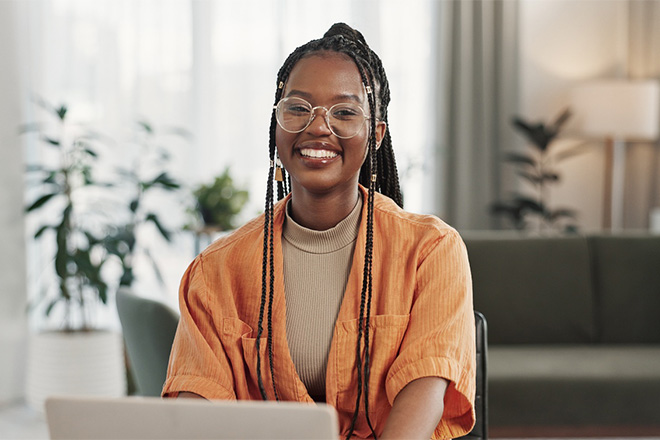 Woman with glasses smiling while working on laptop.